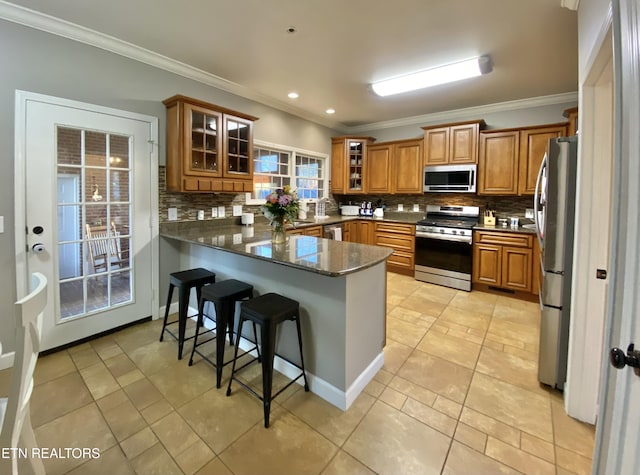 kitchen with backsplash, stainless steel appliances, a kitchen bar, kitchen peninsula, and dark stone counters