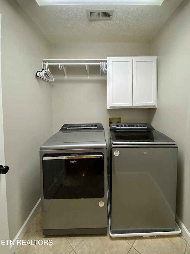 washroom with cabinets, washing machine and dryer, a textured ceiling, and light tile patterned floors