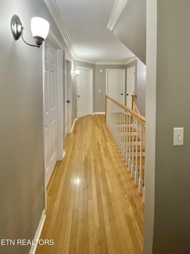 hallway featuring ornamental molding, light wood-type flooring, and baseboards