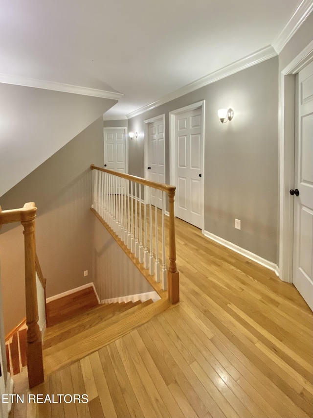 hall with ornamental molding, light wood-type flooring, an upstairs landing, and baseboards