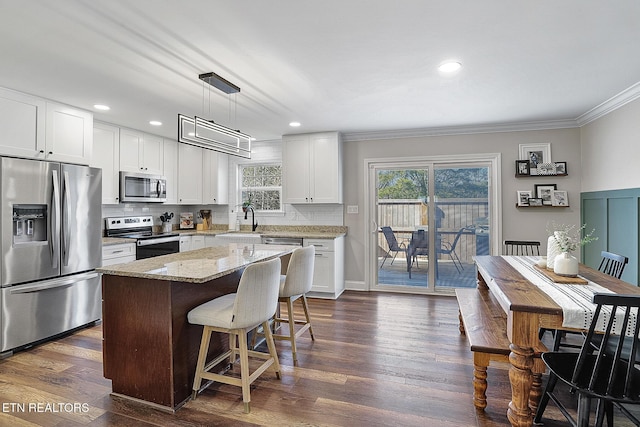 kitchen featuring white cabinetry, decorative light fixtures, stainless steel appliances, and a center island