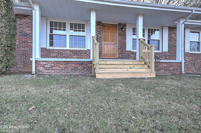 view of exterior entry with covered porch, a lawn, and brick siding