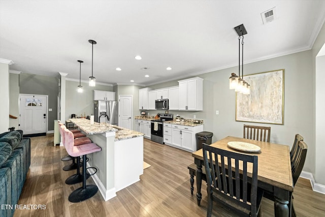 kitchen with appliances with stainless steel finishes, pendant lighting, an island with sink, white cabinets, and light stone countertops