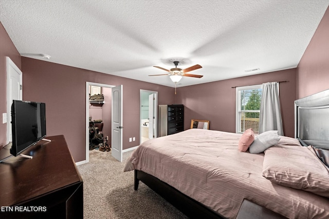 carpeted bedroom featuring a walk in closet, a textured ceiling, ceiling fan, and ensuite bath