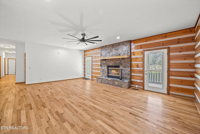 unfurnished living room with ceiling fan, wooden walls, a fireplace, and light hardwood / wood-style flooring