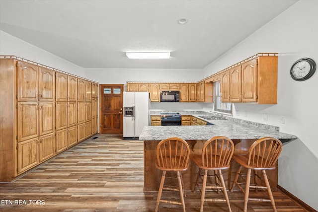 kitchen featuring range with electric cooktop, sink, a kitchen bar, white fridge with ice dispenser, and kitchen peninsula