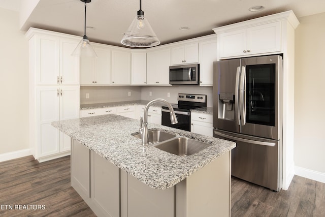 kitchen with decorative light fixtures, stainless steel appliances, white cabinets, and a center island with sink