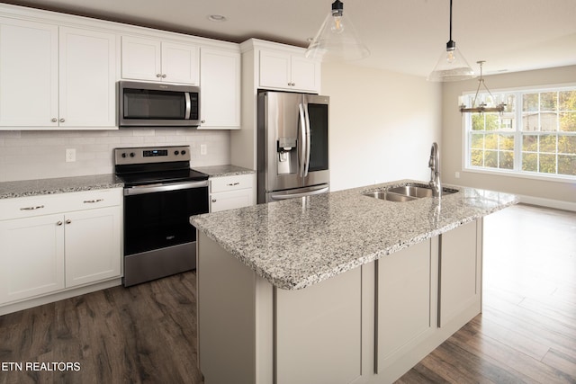 kitchen featuring sink, hanging light fixtures, stainless steel appliances, white cabinets, and a center island with sink