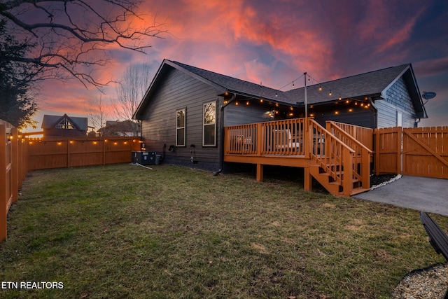 back house at dusk featuring a wooden deck and a yard