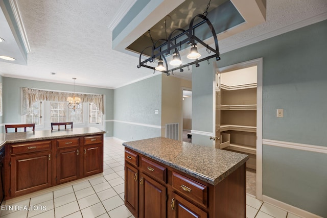 kitchen with crown molding, a center island, a textured ceiling, light tile patterned flooring, and decorative light fixtures