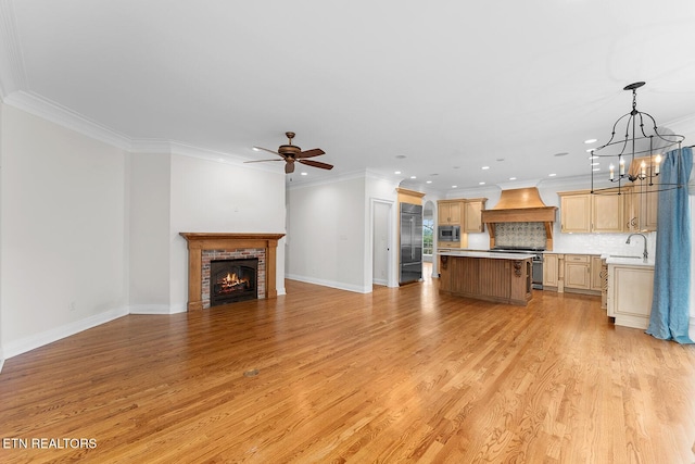 unfurnished living room featuring sink, a brick fireplace, light hardwood / wood-style flooring, ornamental molding, and ceiling fan with notable chandelier