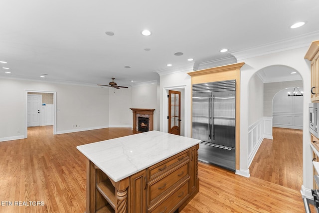 kitchen featuring built in appliances, a brick fireplace, a kitchen island, and light hardwood / wood-style flooring