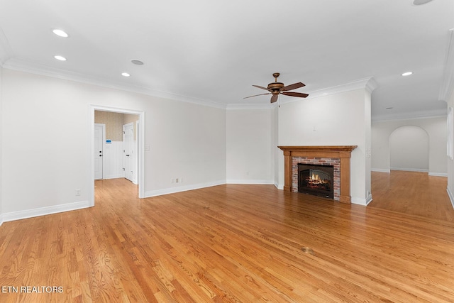 unfurnished living room featuring a brick fireplace, crown molding, ceiling fan, and light wood-type flooring