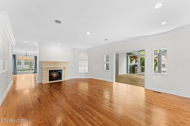 unfurnished living room featuring crown molding, light hardwood / wood-style flooring, and a notable chandelier