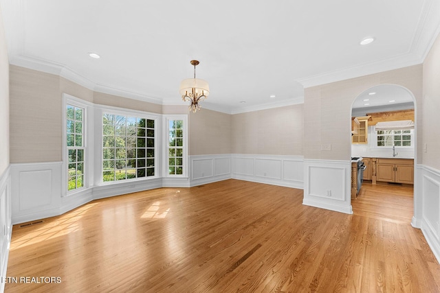 unfurnished dining area with an inviting chandelier, crown molding, and light wood-type flooring