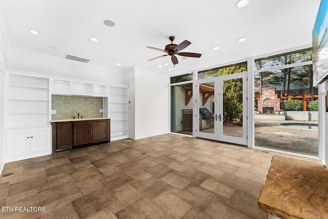 interior space featuring crown molding, built in features, ceiling fan, expansive windows, and french doors