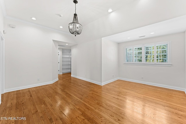 unfurnished room featuring wood-type flooring, crown molding, and an inviting chandelier