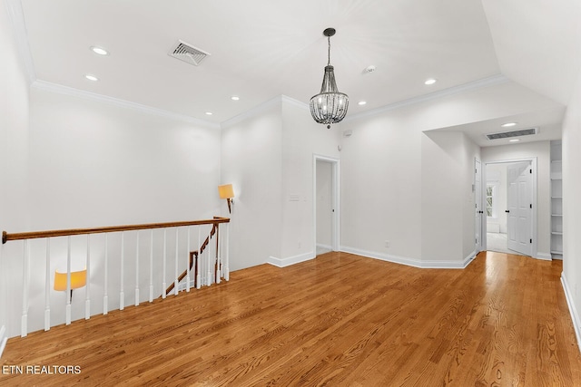 empty room with crown molding, a notable chandelier, and light wood-type flooring