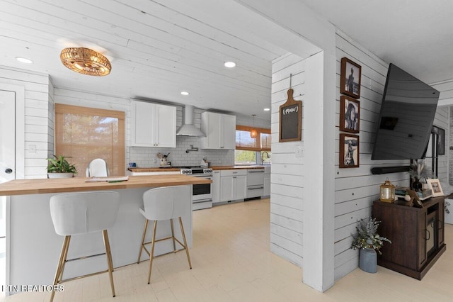 kitchen featuring a breakfast bar, butcher block counters, white cabinetry, stainless steel range oven, and wall chimney exhaust hood