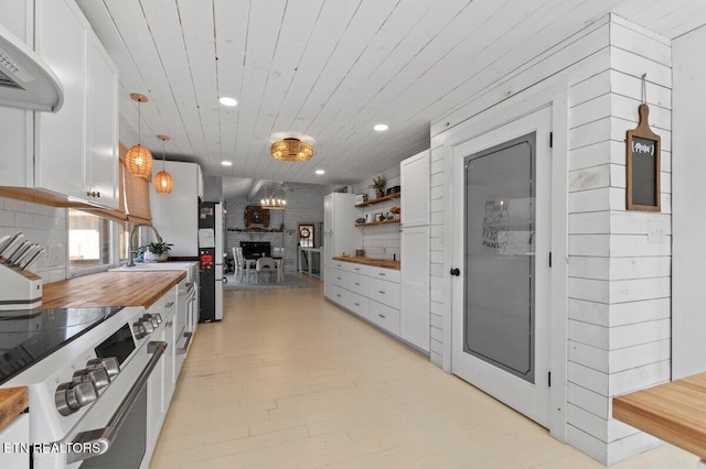 kitchen with butcher block counters, stainless steel electric range, pendant lighting, and white cabinets