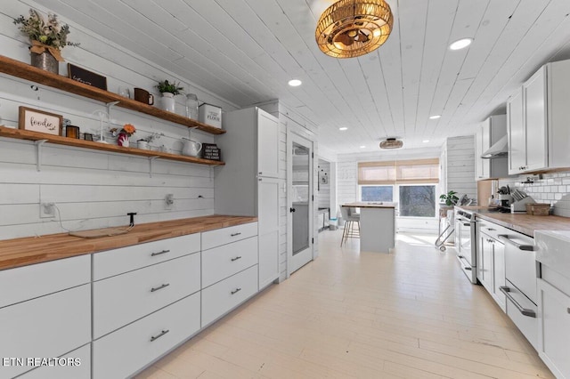 kitchen featuring butcher block countertops, wood ceiling, white cabinetry, backsplash, and stainless steel range oven