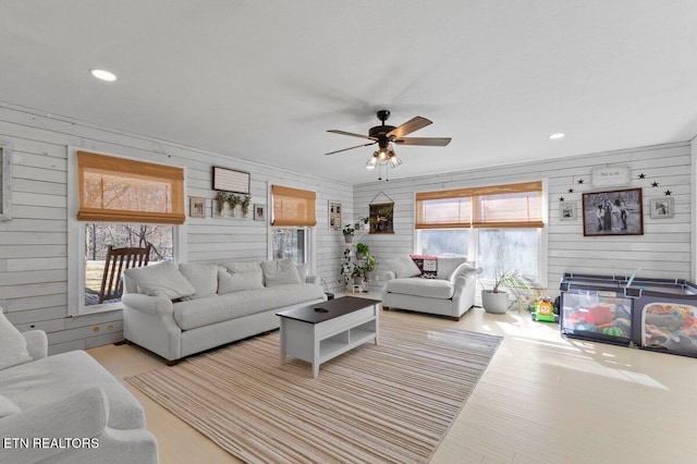 living room featuring ceiling fan, wooden walls, and light wood-type flooring