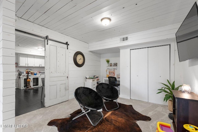 interior space featuring light carpet, wood ceiling, a barn door, and wood walls