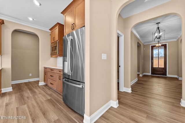 kitchen featuring crown molding, an inviting chandelier, decorative light fixtures, stainless steel appliances, and light hardwood / wood-style floors