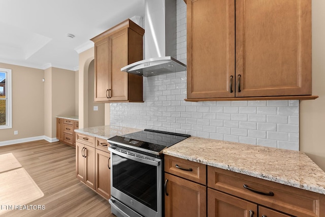 kitchen featuring light stone counters, stainless steel electric range oven, decorative backsplash, wall chimney exhaust hood, and light wood-type flooring