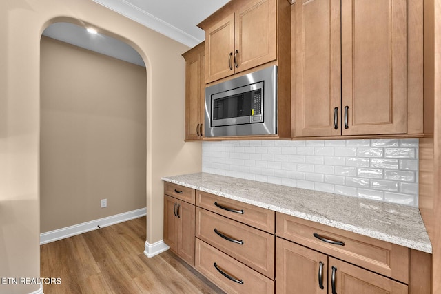 kitchen with light hardwood / wood-style flooring, stainless steel microwave, tasteful backsplash, ornamental molding, and light stone countertops