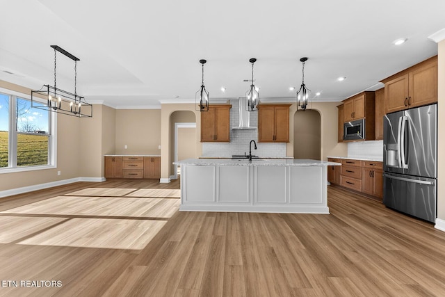 kitchen featuring pendant lighting, appliances with stainless steel finishes, a kitchen island with sink, and wall chimney range hood