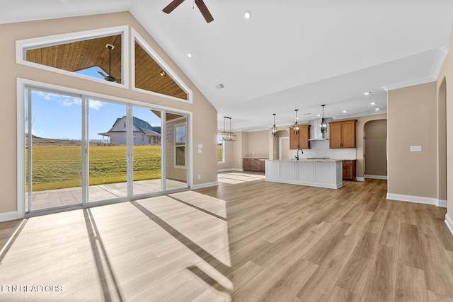 unfurnished living room with sink, light hardwood / wood-style flooring, high vaulted ceiling, ornamental molding, and ceiling fan with notable chandelier