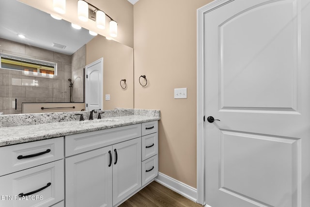 bathroom with hardwood / wood-style flooring, vanity, and a tile shower