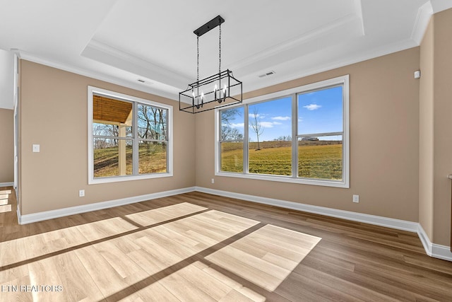 unfurnished dining area featuring ornamental molding, hardwood / wood-style floors, an inviting chandelier, and a tray ceiling