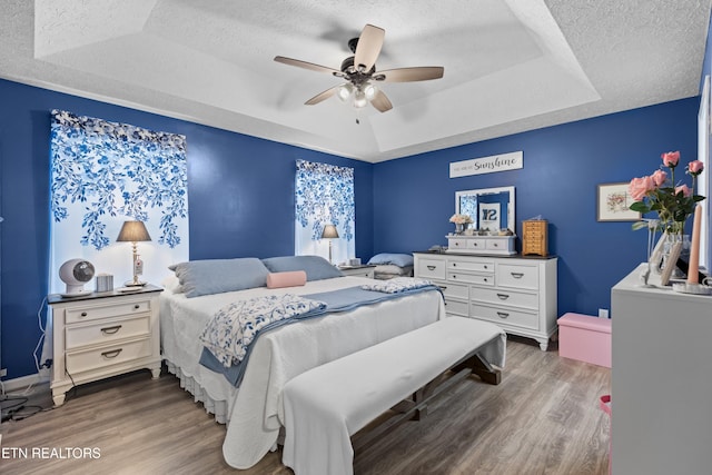 bedroom featuring dark hardwood / wood-style flooring, ceiling fan, a tray ceiling, and a textured ceiling