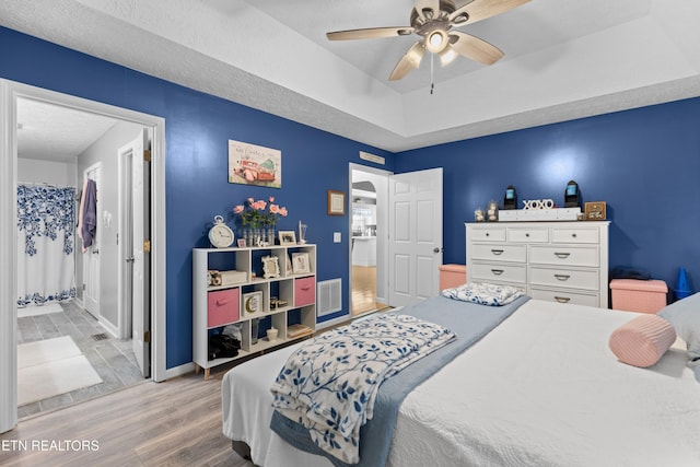 bedroom featuring ceiling fan, a raised ceiling, a textured ceiling, and light wood-type flooring