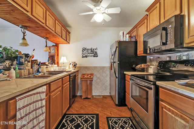 kitchen with decorative light fixtures, black appliances, sink, ceiling fan, and light hardwood / wood-style floors