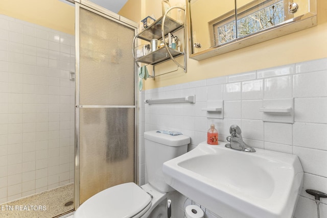 bathroom with walk in shower, toilet, sink, and tile walls