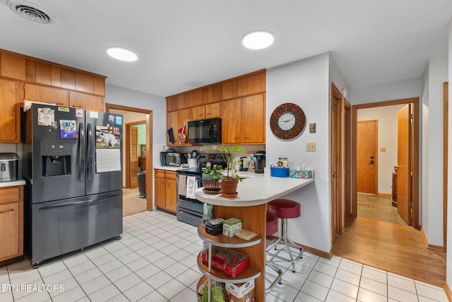 kitchen with kitchen peninsula, light tile patterned floors, a breakfast bar area, and black appliances