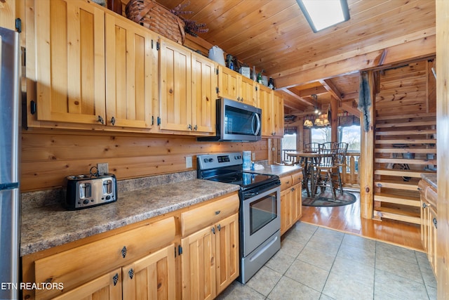 kitchen featuring light tile patterned floors, beam ceiling, wooden walls, stainless steel appliances, and wooden ceiling