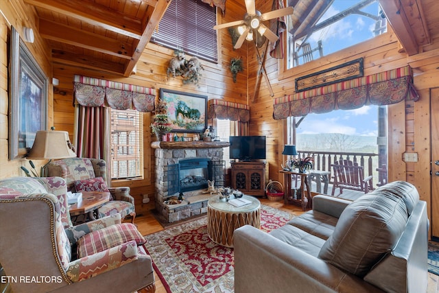 living room featuring beam ceiling, wooden walls, wooden ceiling, and a stone fireplace