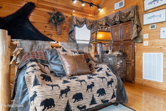 bedroom featuring hardwood / wood-style flooring, rail lighting, lofted ceiling, and wood walls