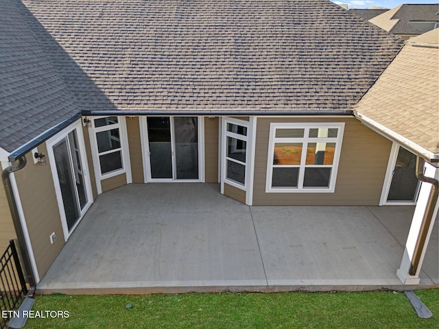 property entrance with a shingled roof and a patio