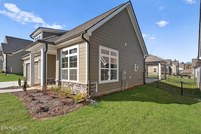 view of home's exterior with a garage, stone siding, a residential view, fence, and a yard