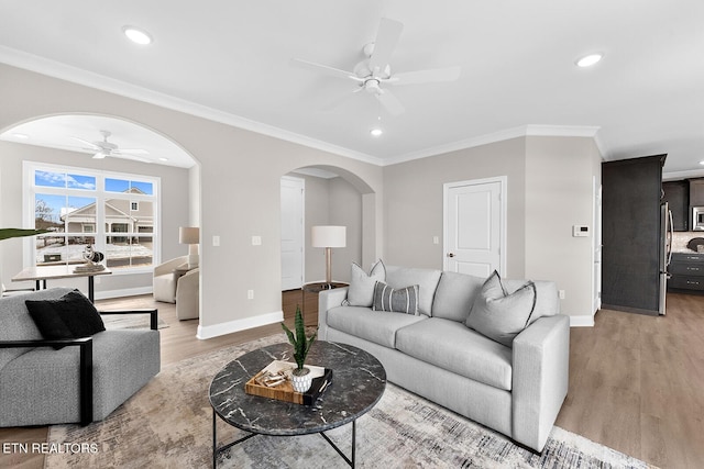 living room with arched walkways, ceiling fan, ornamental molding, and light wood-style flooring