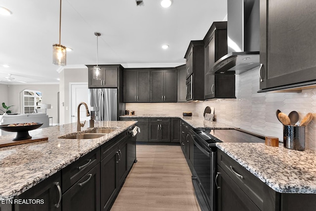 kitchen with hanging light fixtures, a sink, black appliances, an island with sink, and wall chimney exhaust hood