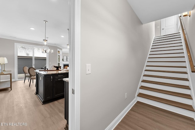 stairway featuring a warm lit fireplace, recessed lighting, wood finished floors, and baseboards