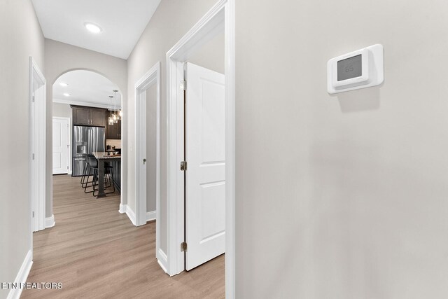 hall with light wood-style floors, arched walkways, baseboards, and recessed lighting