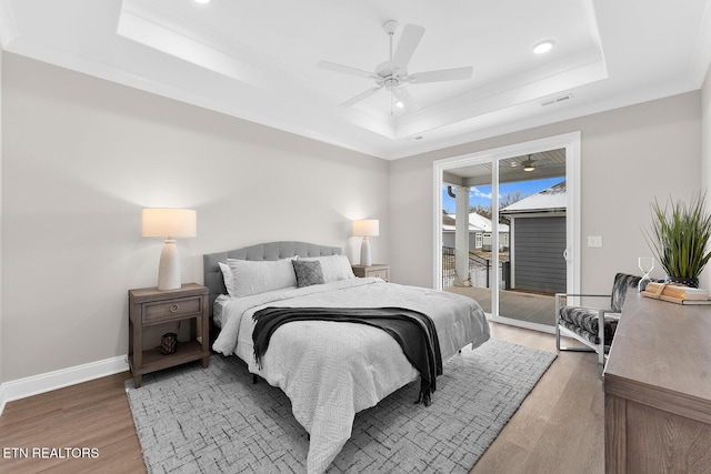 bedroom with baseboards, access to outside, a tray ceiling, and wood finished floors