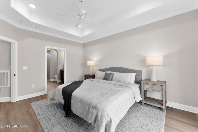 bedroom featuring wood finished floors, a raised ceiling, and baseboards